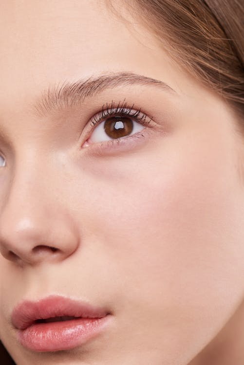 Woman with a clean, bare face showing natural skin tone, lips, and brows — no makeup, clear and even lighting